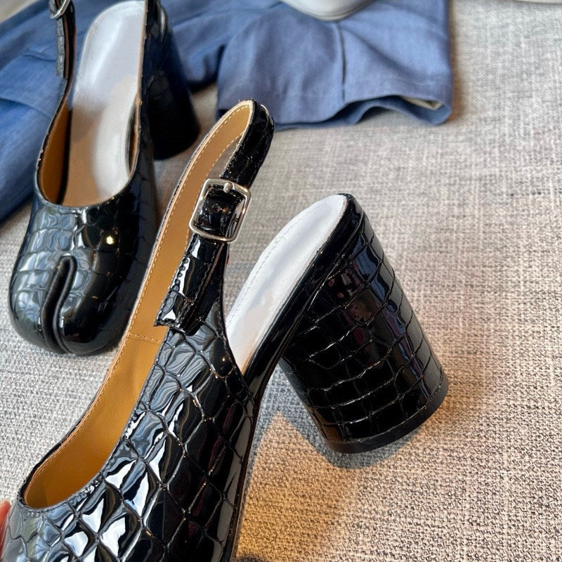 Black crocodile-patterned high-heeled shoes on a textured surface