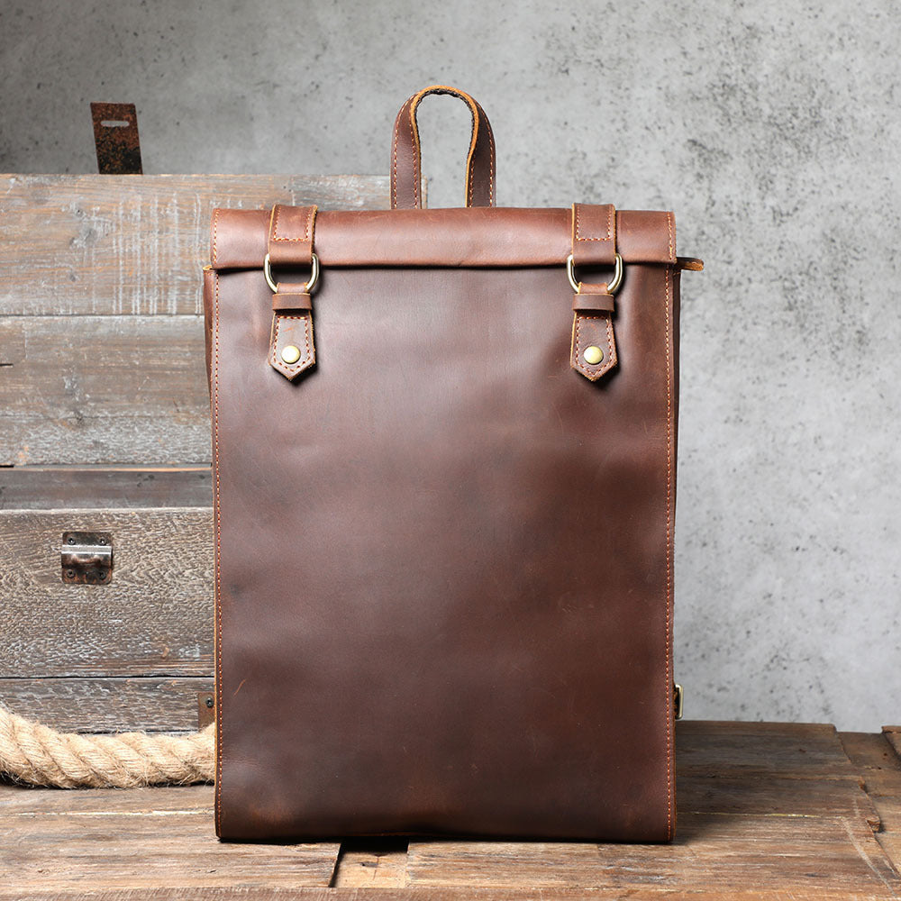 Brown leather backpack on a wooden surface with a concrete wall background