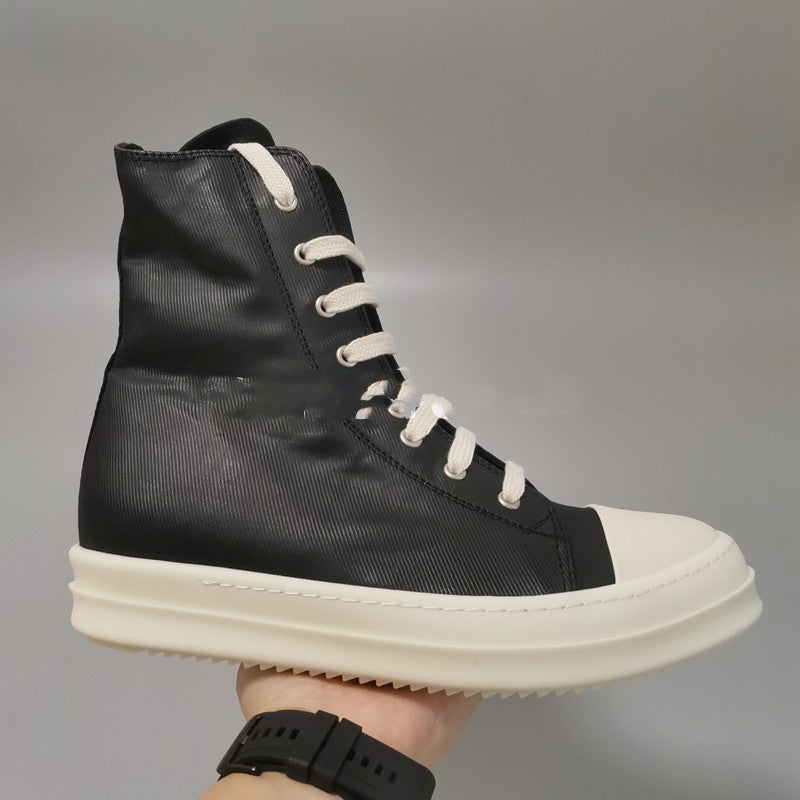 Black high-top sneaker with white laces and sole held by a hand against a gray background