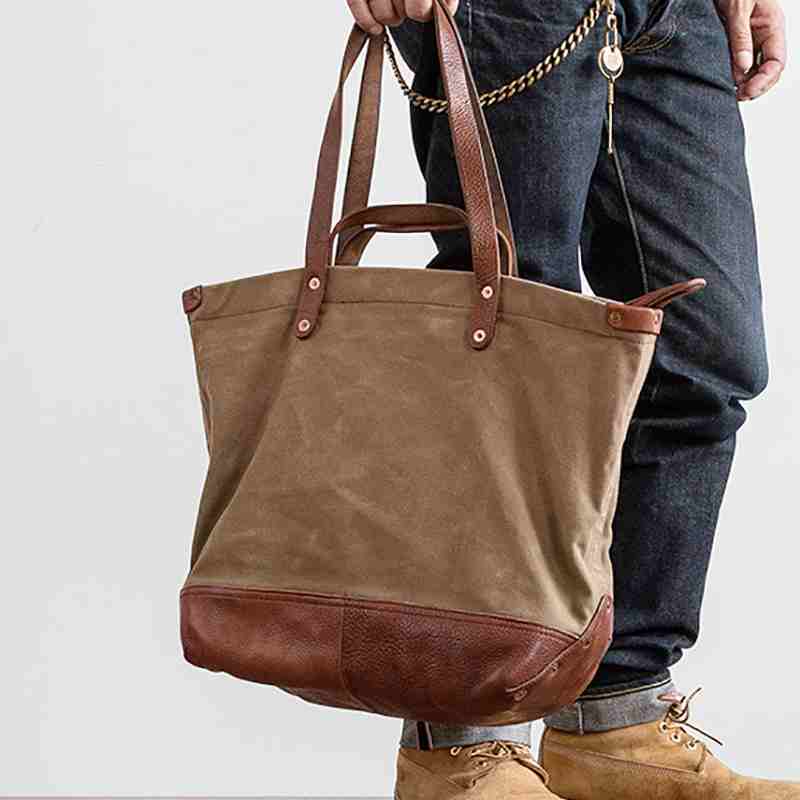 Brown tote bag with leather accents held by a person against a white background