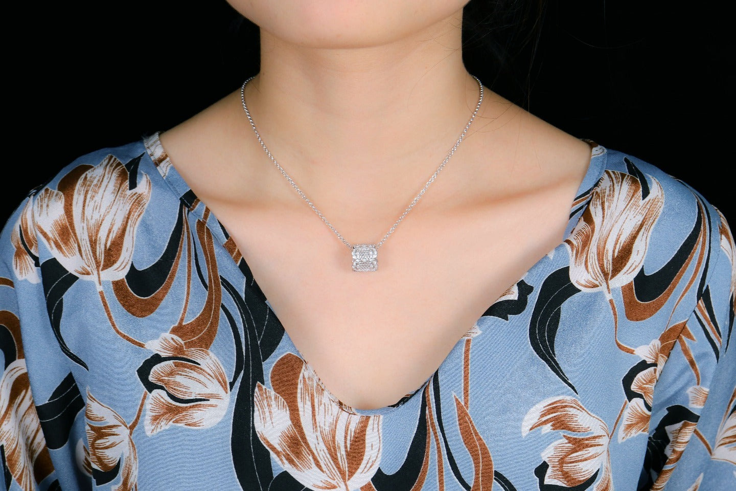 Necklace with a square pendant worn by a person against a floral-patterned garment.