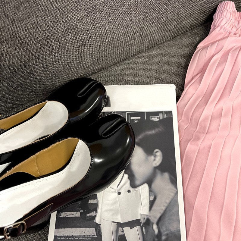 Black and white shoes on a magazine with a pink fabric item next to them.