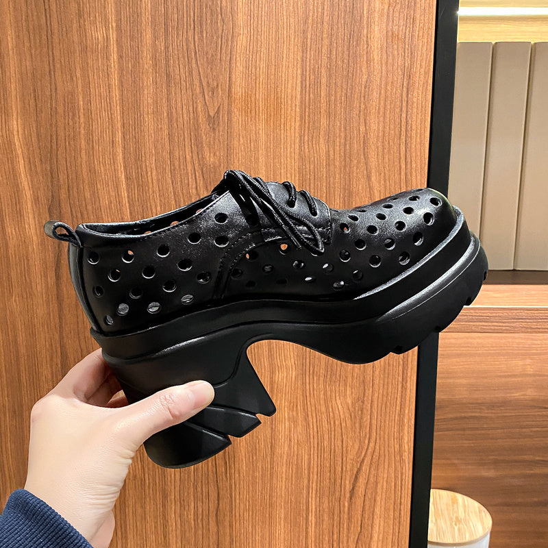 Black shoe with holes held by a hand against a wooden background