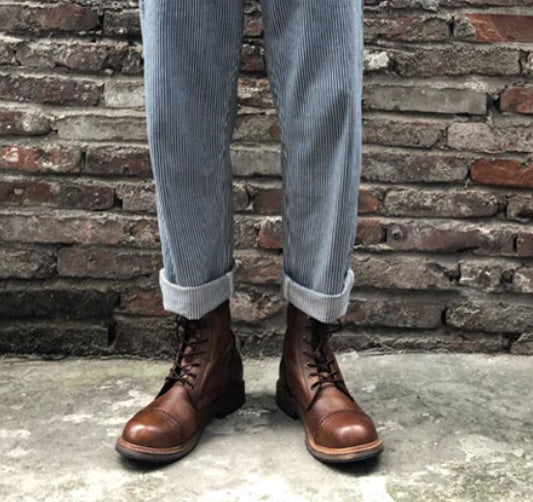 Brown leather boots worn with light blue jeans against a brick wall.