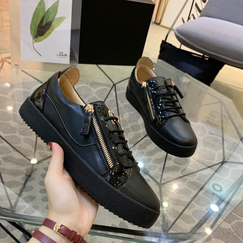Black sneakers with gold zippers held by a hand on a reflective surface.