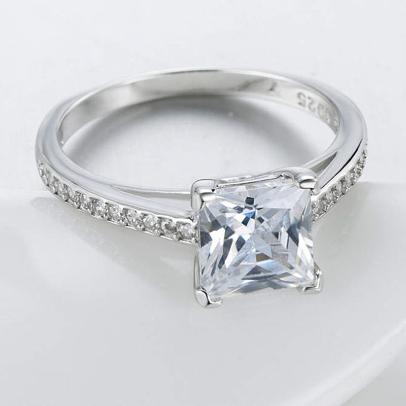 Silver ring with a large diamond and smaller diamonds on the band against a light background