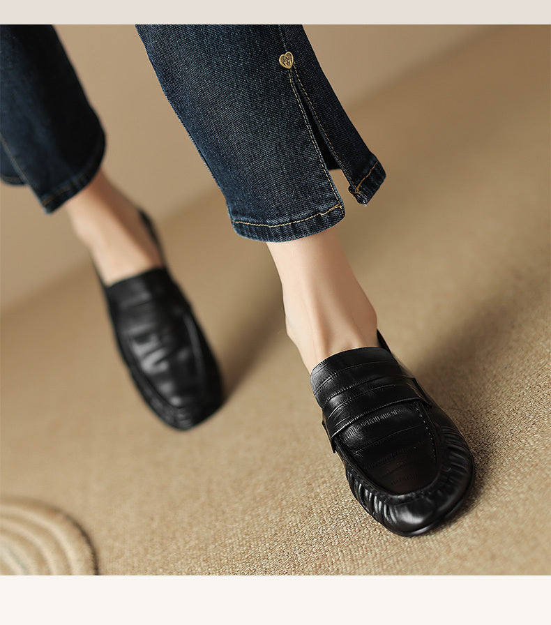 Black loafers worn with blue jeans on a beige surface