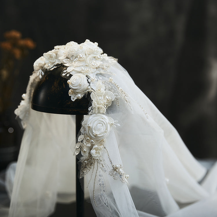 White floral headpiece with veil on a black stand against a dark background