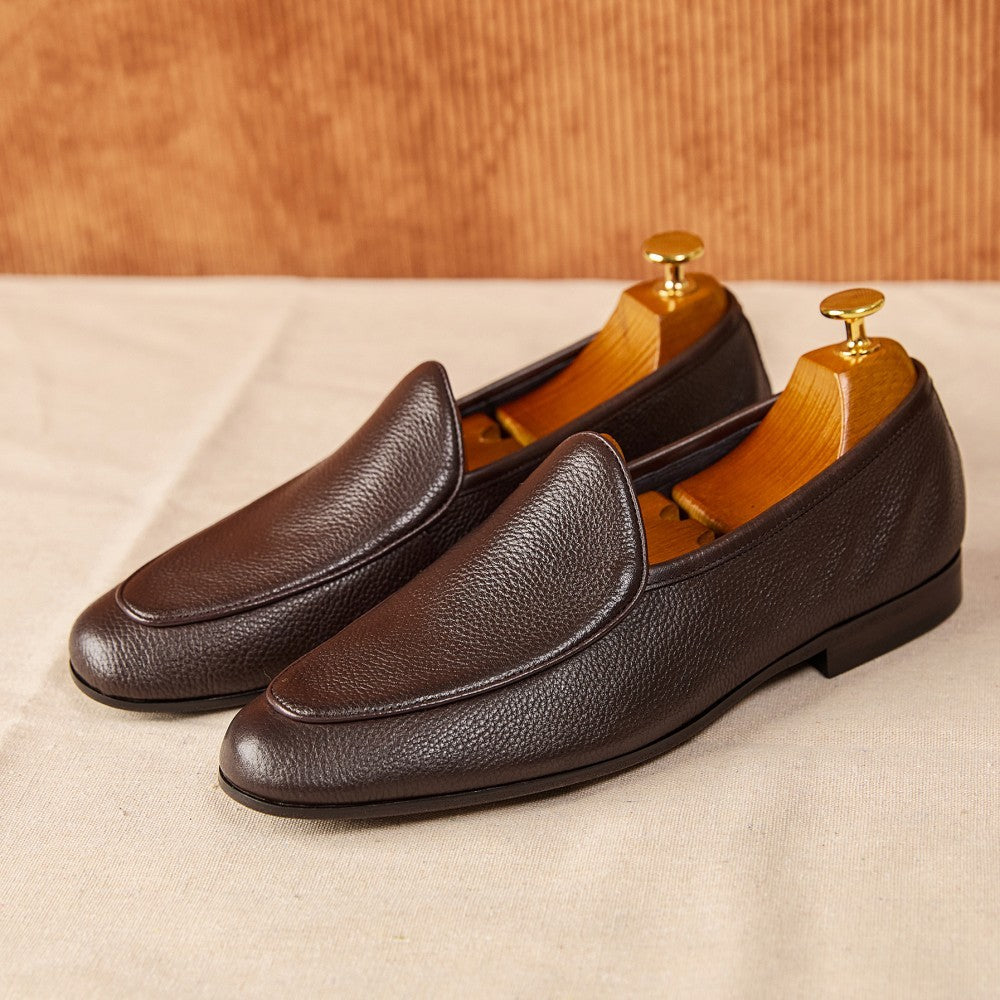 Pair of brown leather loafers on a beige surface with a wooden background