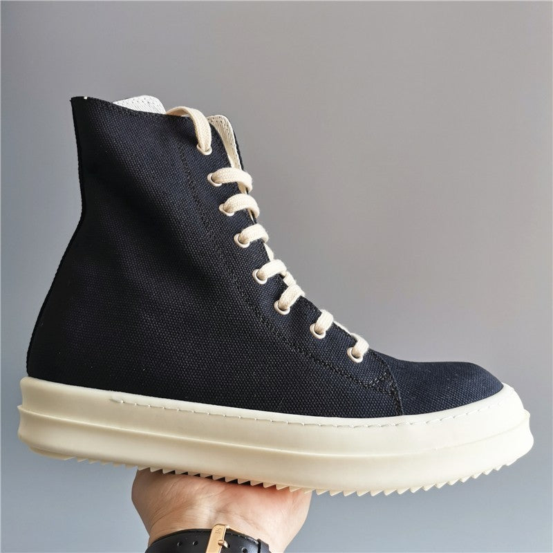 Black high-top sneaker with white sole held by a hand against a gray background