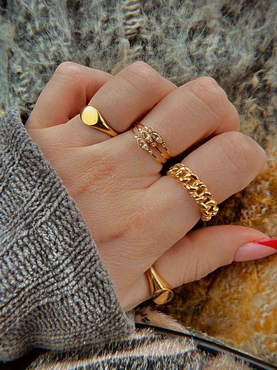 Hand wearing multiple gold rings on a textured surface