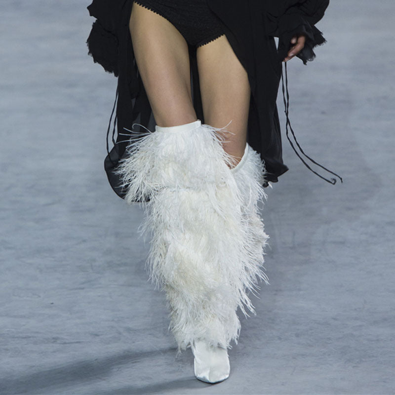 White feathered boots worn by a model on a gray runway.