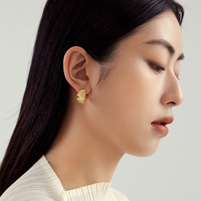 Close-up of a woman wearing a gold earring against a neutral background