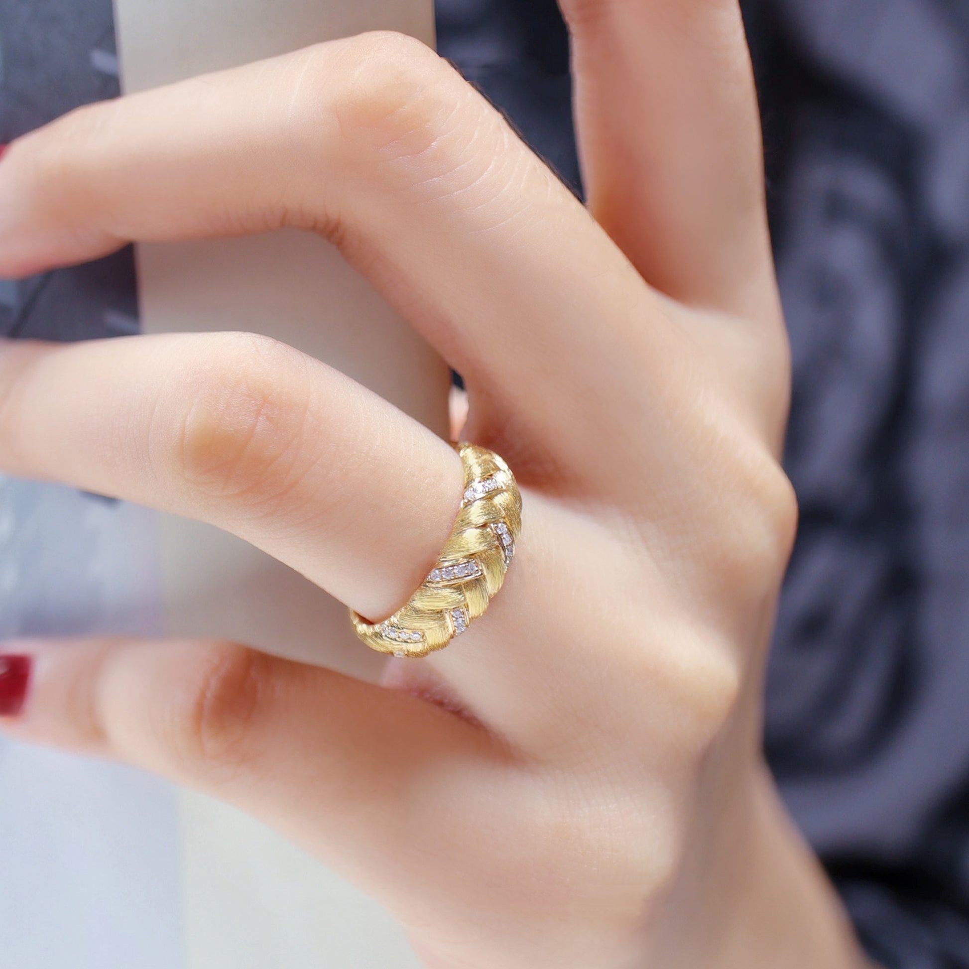 Gold ring with diamonds on a person's finger against a neutral background