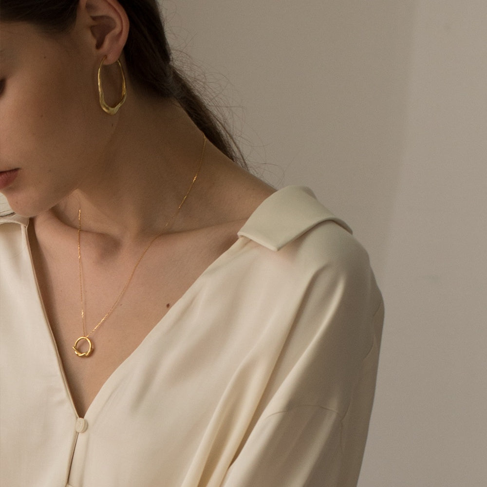 Woman wearing gold hoop earrings and a necklace against a neutral background