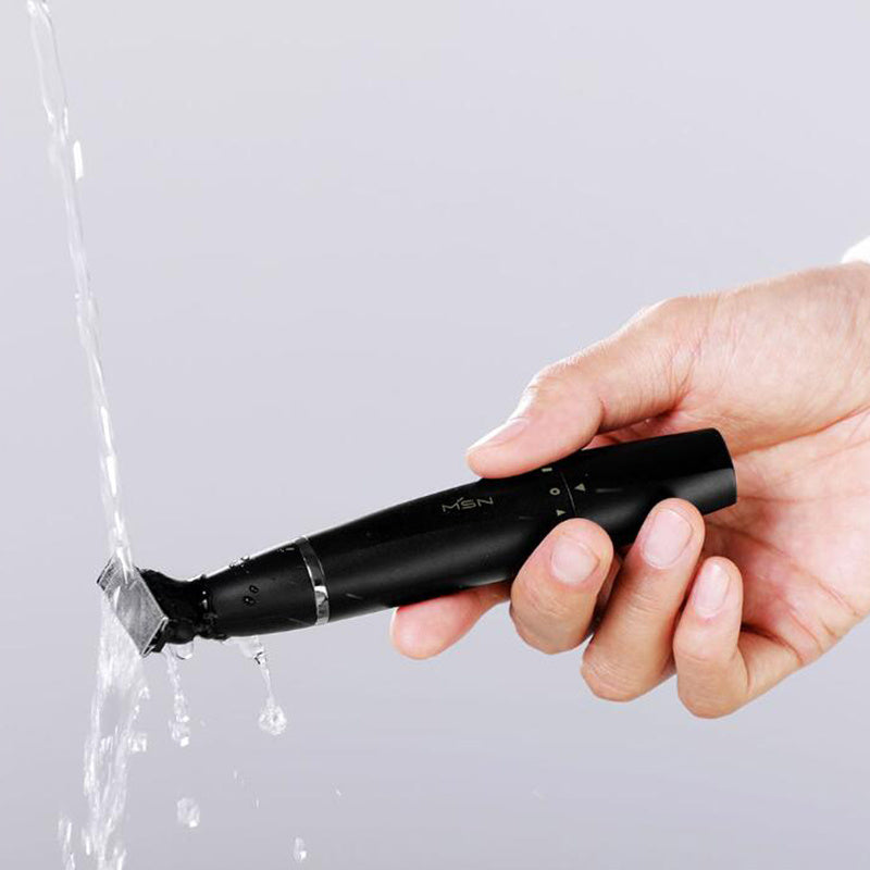 Hand holding a black electric shaver with water splashing around it on a light gray background