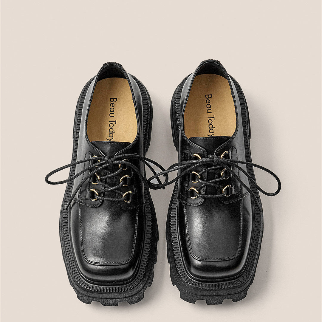 Pair of black leather shoes with thick soles on a beige background