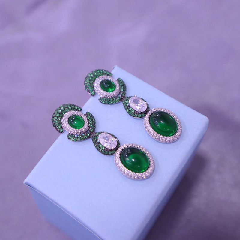 Green gemstone earrings on a white jewelry box with a purple background