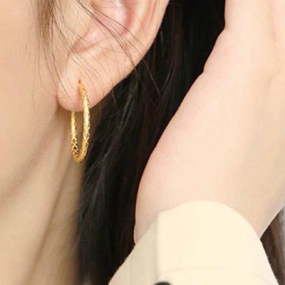 Gold hoop earring worn by a person with dark hair.