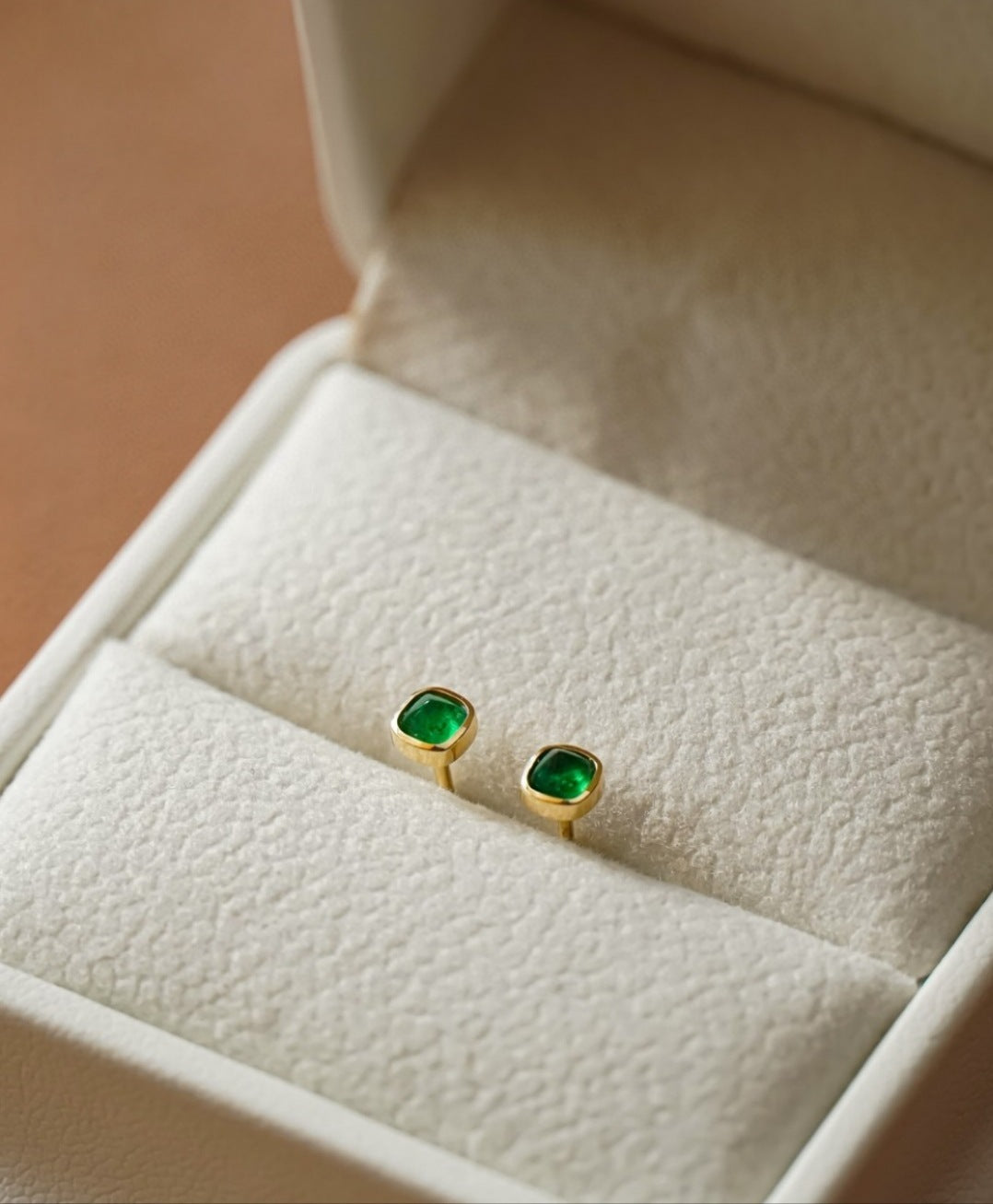 Gold earrings with green gemstones in a jewelry box
