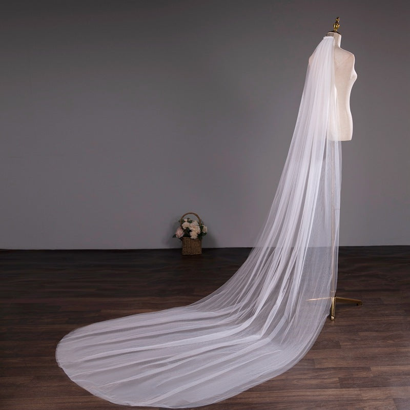 Long white wedding veil on a mannequin against a gray wall.
