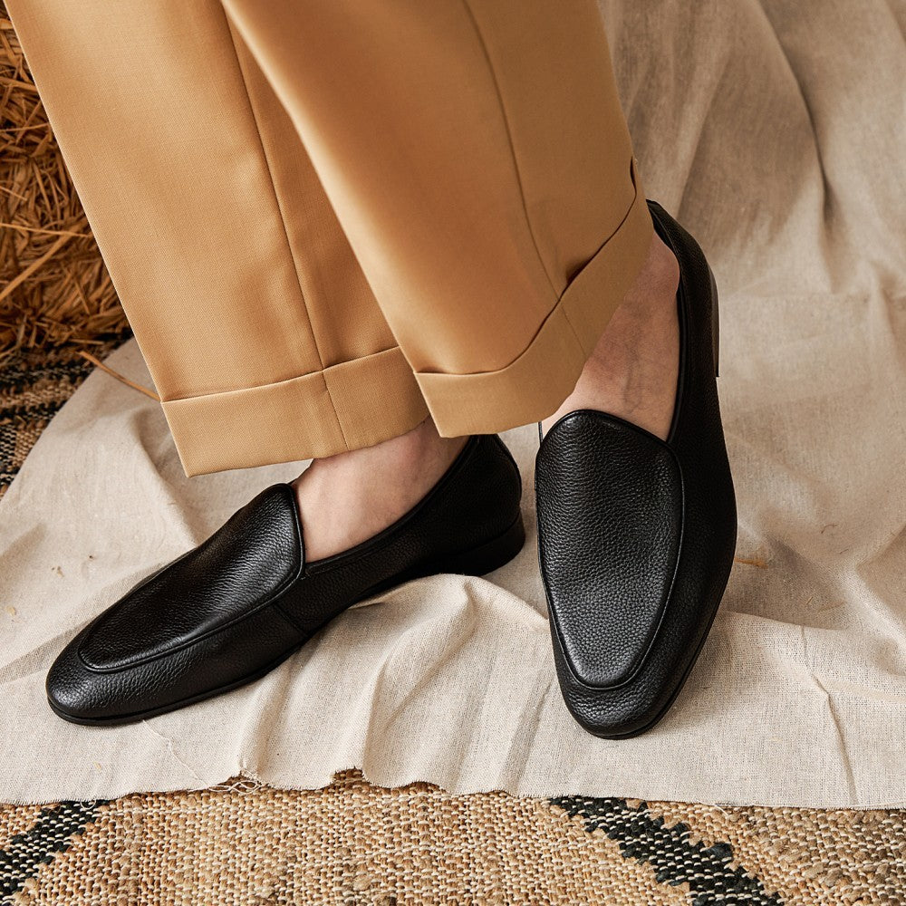 Black loafers worn with beige pants on a textured surface