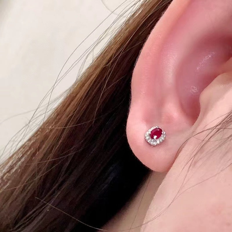 Close-up of an ear wearing a red gemstone earring with a white border.