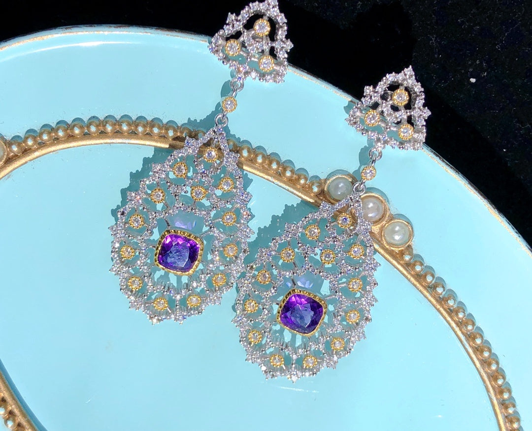 Ornate earrings with purple gemstones on a light blue plate