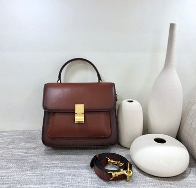 Brown handbag with gold accents on a textured surface with white vases.