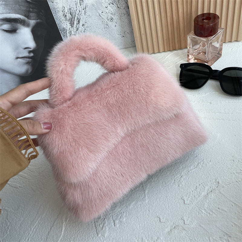 Pink fluffy handbag held by a person with sunglasses and a bottle of perfume in the background.