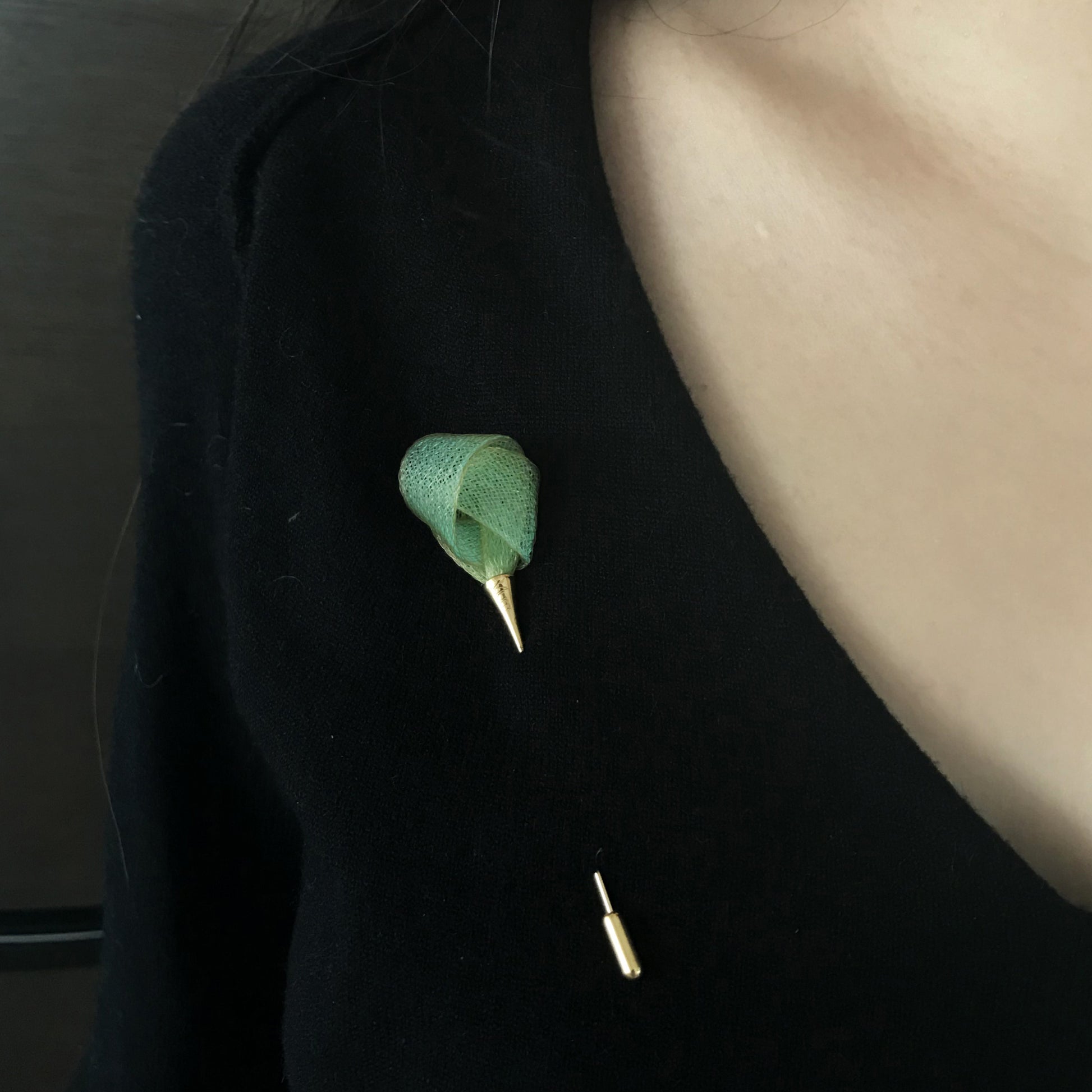 Green leaf-shaped brooch on a black coat with a blurred background
