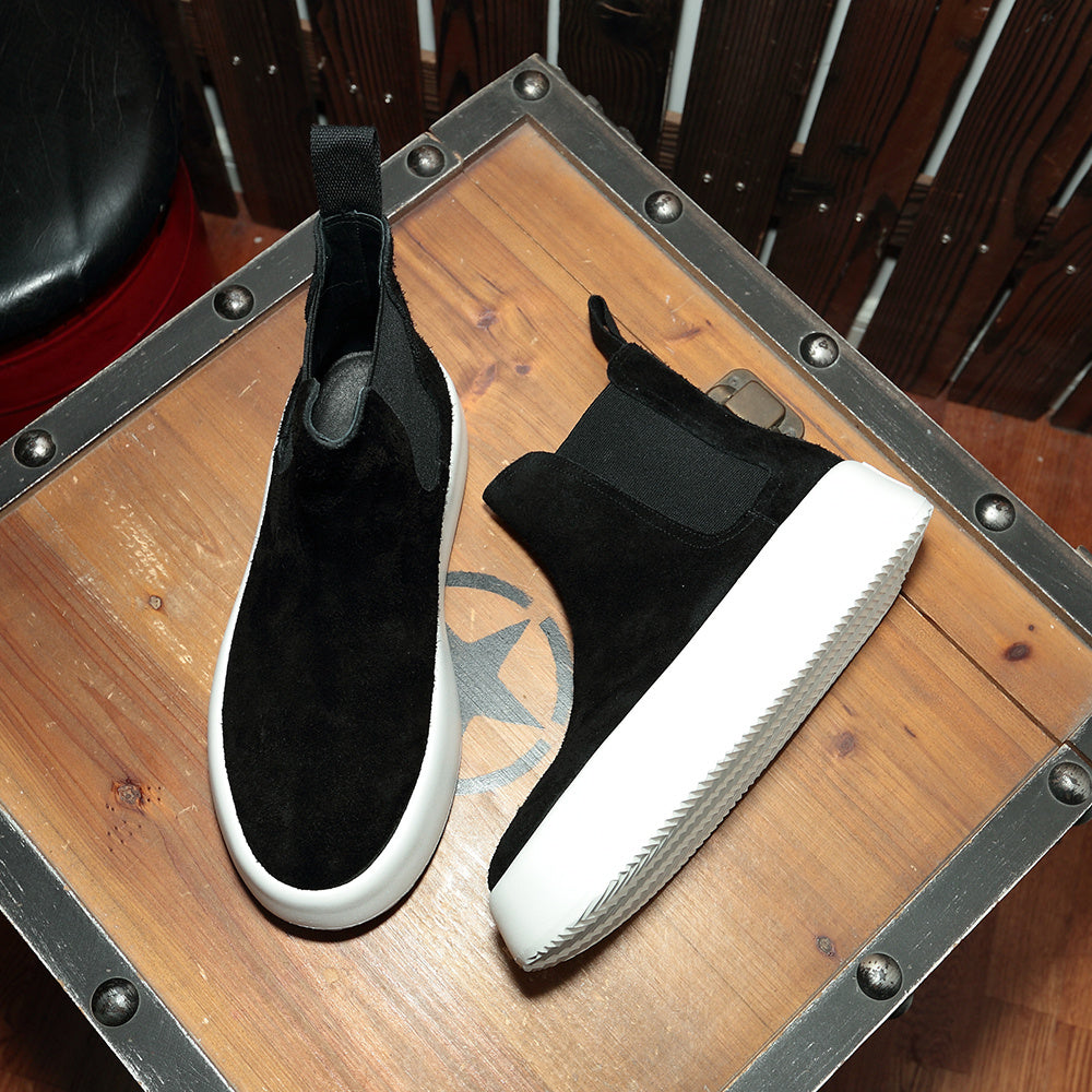 Black slip-on shoes with white soles on a wooden surface