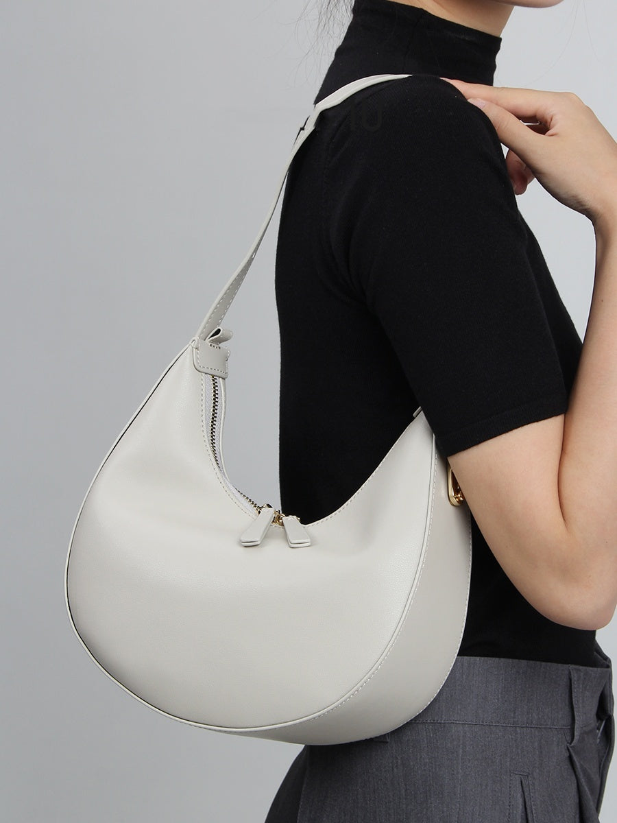 Person wearing a white handbag over one shoulder against a gray background