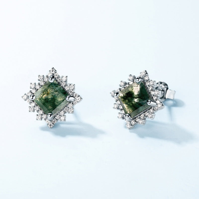Pair of earrings with green gemstones and diamond-like accents on a light background