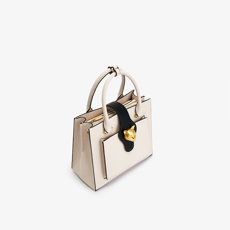 Beige handbag with black strap and gold hardware on a white background