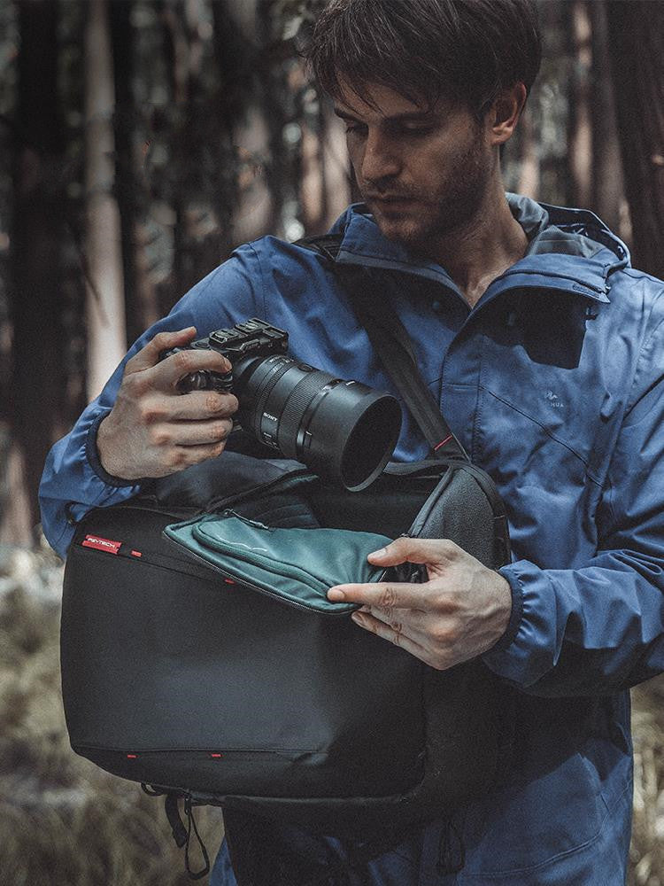 Man in blue jacket holding a camera and bag in a forest setting