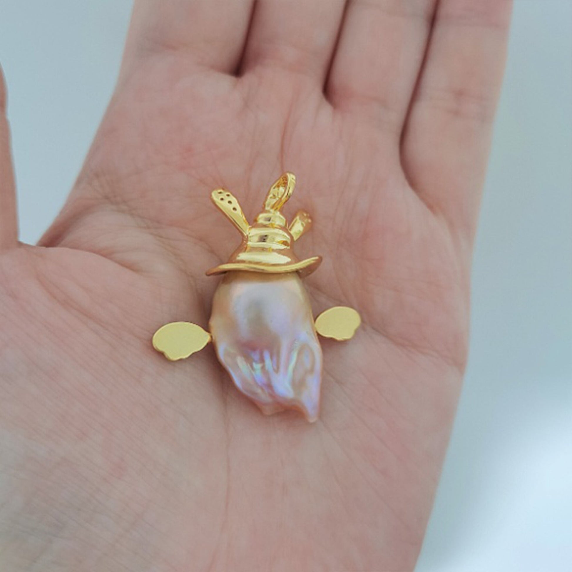 Gold pendant with a shell on a hand against a white background