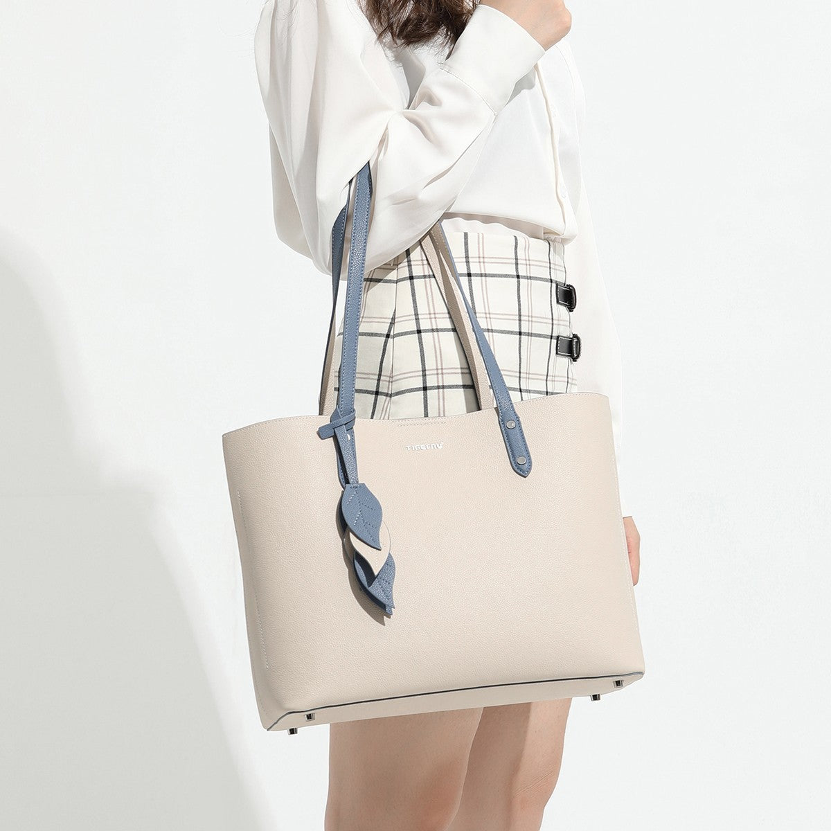 Person holding a beige tote bag with blue straps on a white background