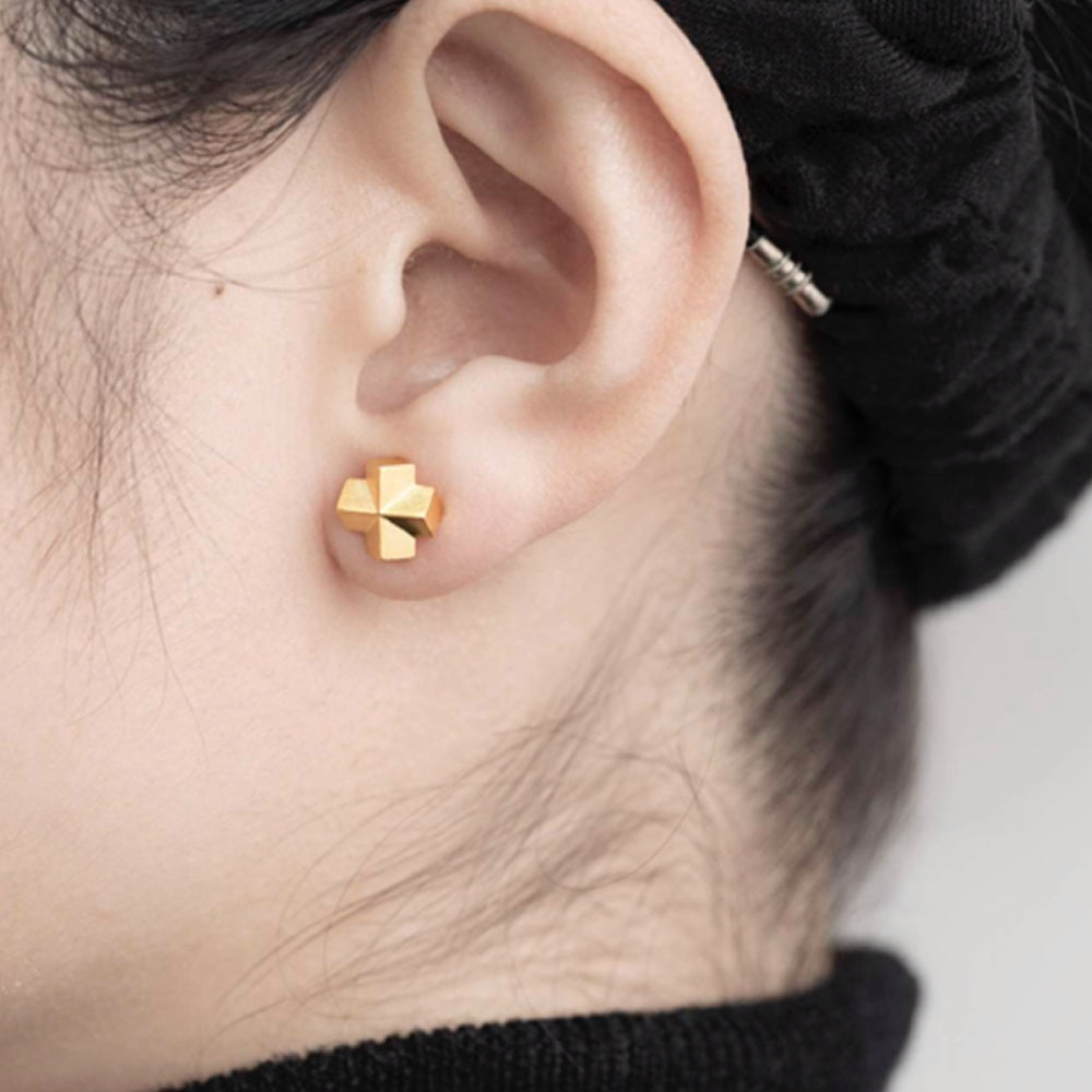 Gold cross-shaped earring worn by a person with a blurred background