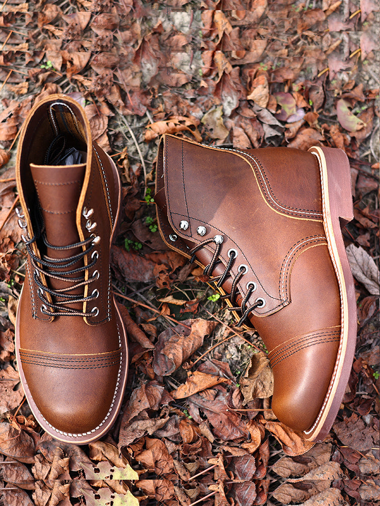 Pair of brown leather boots on a ground covered with fallen leaves.
