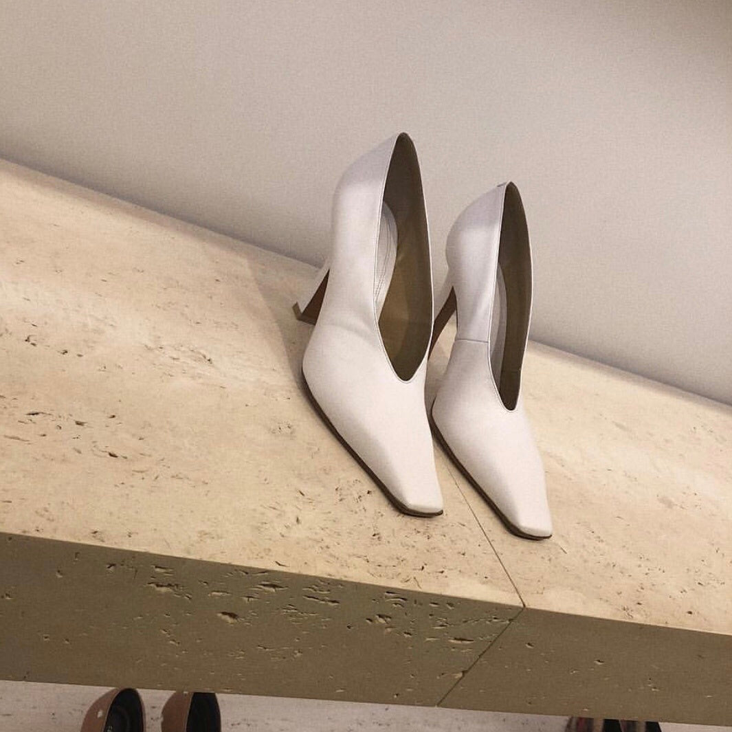 White high-heeled shoes on a light wooden surface with a neutral background