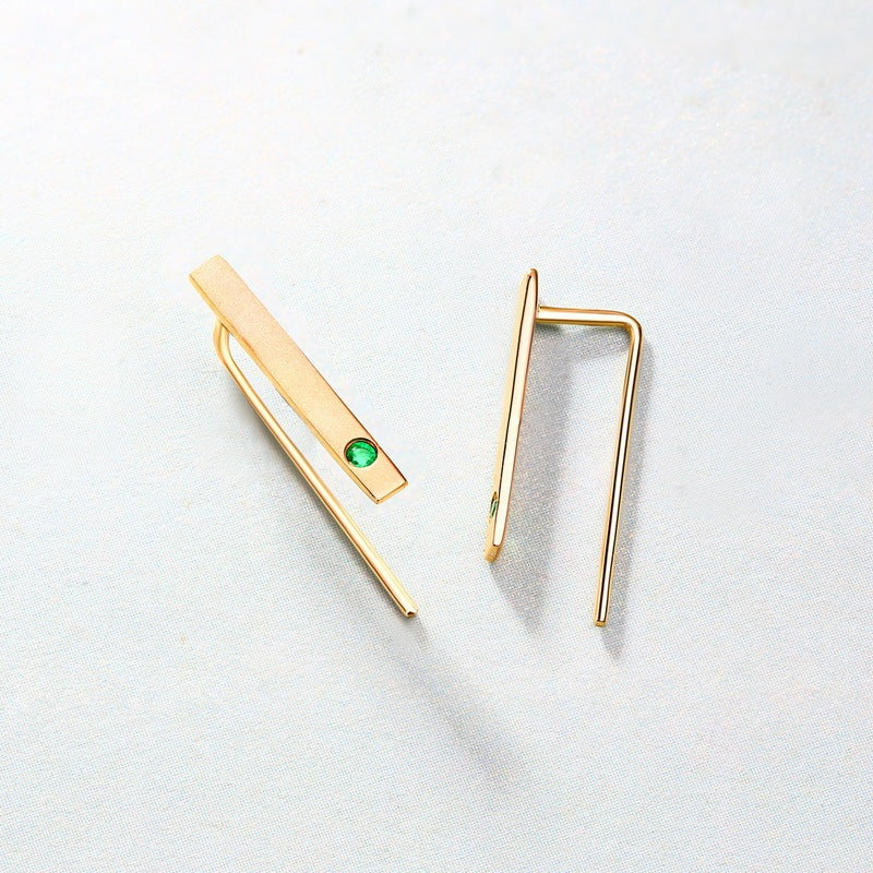 Gold earrings with a green gemstone on a light gray background