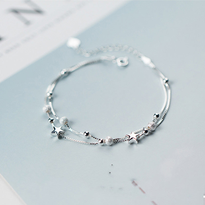 Silver bracelet with star and moon charms on a light blue surface