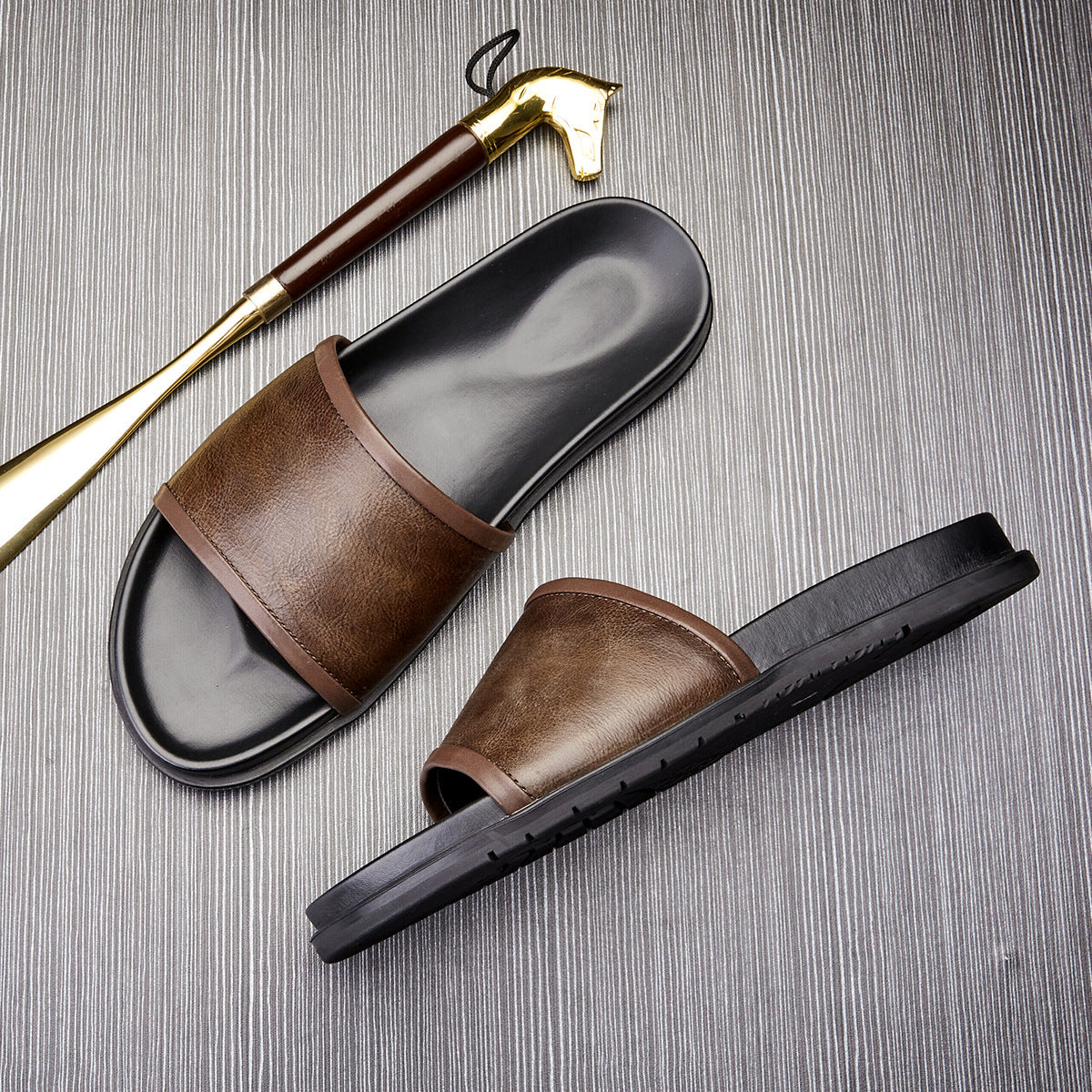 Brown leather slides with black soles on a textured surface