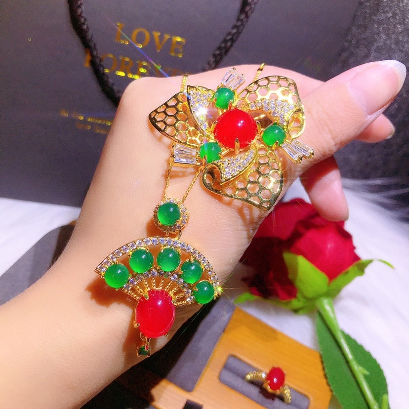 Decorative brooch with red and green gemstones held by a hand, with a blurred background.
