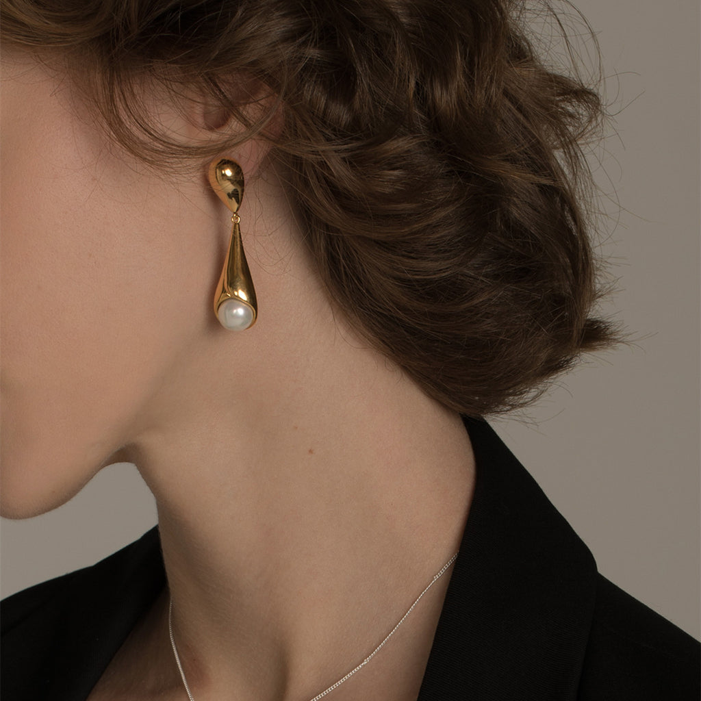 Gold earring with pearl detail on a model against a neutral background
