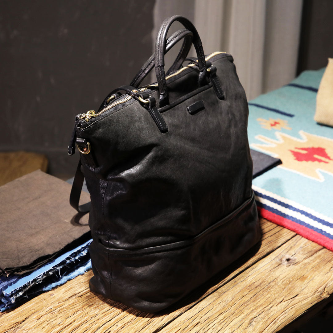 Black leather backpack on a wooden surface with a colorful blanket in the background