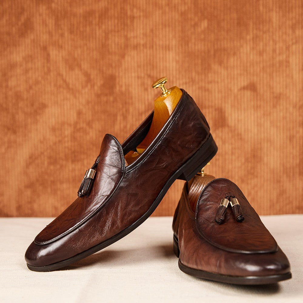 Pair of brown leather loafers with tassels on a beige surface and brown background