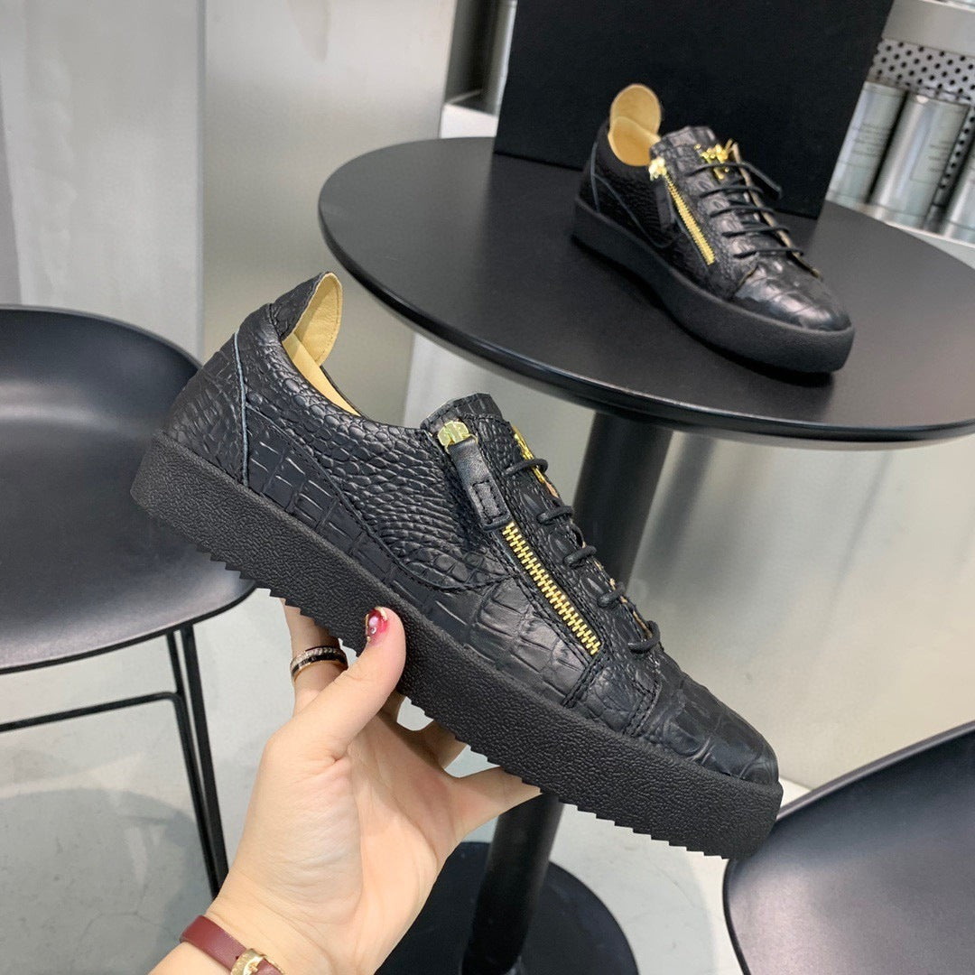Black textured sneaker with yellow accents held by a hand, with another sneaker on a small round table in the background.