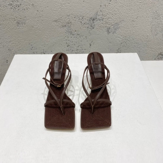 Pair of brown sandals on a white platform with a gray concrete background